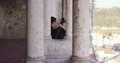 Pro surfer Nuno Santos playing Cello at balcony of Leiria castle on bright day Stock Footage 155265998