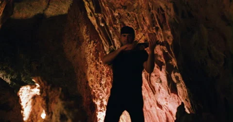 Pro surfer Nuno Santos walking inside underground caves and playing violin Stock Footage 155257538