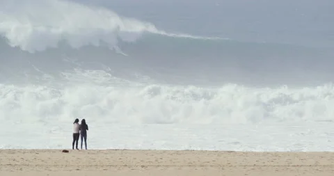 Pro surfer riding big waves in ocean and people watching him from beach Stock Footage 149943400