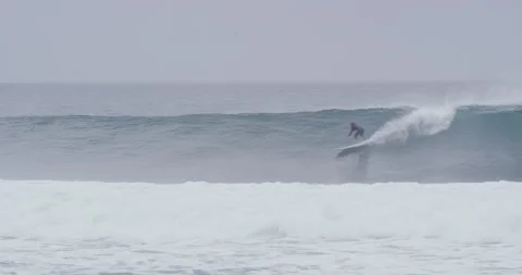 Pro surfer riding down fast ocean wave while others are watching on cloudy day Stock Footage 156015767