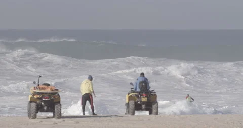 Pro surfer riding wild waves in ocean on jet skis on sunny day in Nazare Stock Footage 160758292