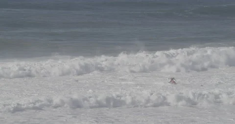 Pro surfer walking on sandy beach next to ocean with big waves splashing Stock Footage 160766472