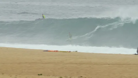 Pro surfers riding big waves on surfboards in ocean near beach with people 스톡 동영상 155596713