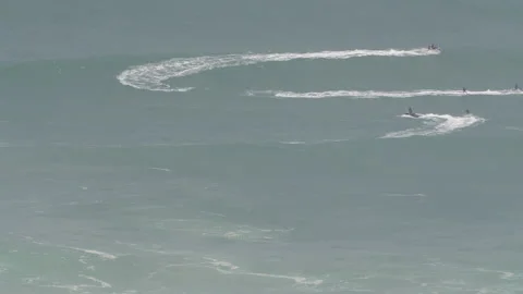 Pro  surfers riding waves in ocean on jet skis on sunny day in Nazare Stock Footage 157697946