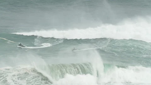 Pro surfers riding wild waves in ocean on jet skis on sunny day in Nazare Stock Footage 157698676