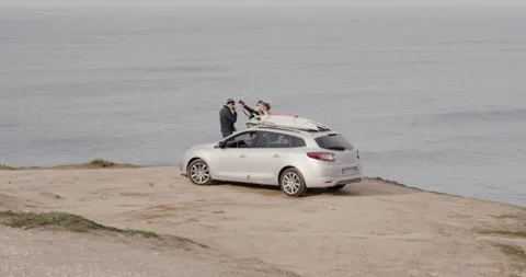 Pro surfers taking selfies next to car with wavy ocean in background Stock Footage 164322577