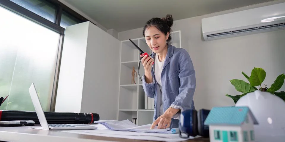 Proactive Female Engineer Coordinating Projects Over Radio Amid Architectural Stock Photos