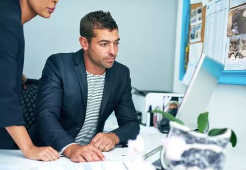 Problem solving is their specialty. two coworkers working together at a computer Stock Photos
