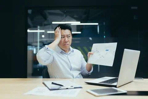 Problems with documents at work. Serious young Asian businessman, broker shows Stock Photos