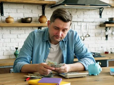 Problems with home finances. The man is counting money in the apartment. Stock Photos