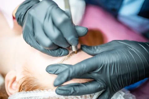 Procedure of eyebrow microblading. A master in black gloves is doing a blending Stock Photos