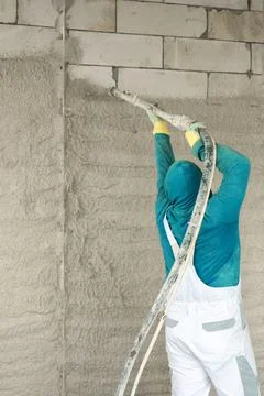 The process of applying plaster to walls inside a building by machine. Stock Photos