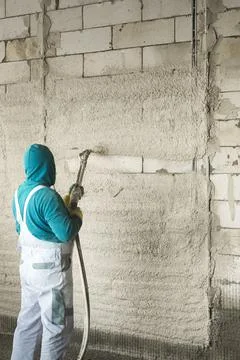 The process of applying plaster to walls inside a building by machine. Stock Photos