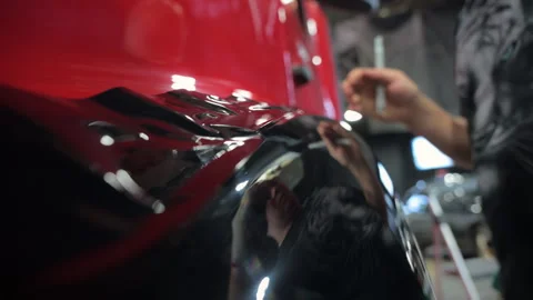 Process of applying a PPF film to a car. Worker removes the rest of PPF film Stock Footage 294963689