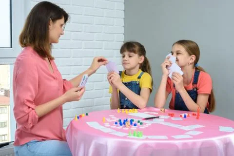 In the process of a board game, mom chooses a card from her daughters hand Stock Photos