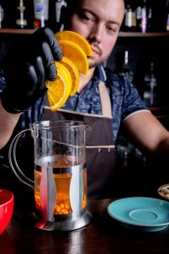Process brewing tea,tea ceremony. Bartender adds sliced orange into the kettle Stock Photos