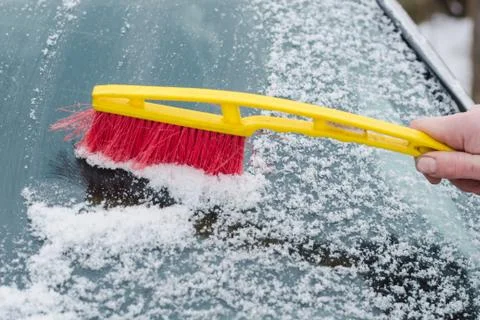 The process of cleaning the windshield of the car from the snow with a red an Stock Photos