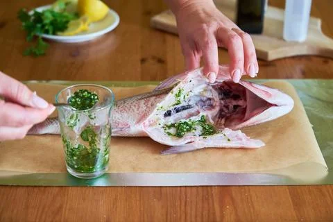 Process of cooking Dorado fish with olive oil and herbs. Female hands close-up. Stock Photos