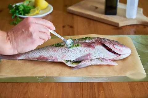 Process of cooking Dorado fish with olive oil and herbs. Female hands close-up. Stock Photos