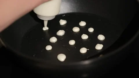 Process of cooking tiny mini pancake cereal. Dough is poured into hot pan Stock Footage 150588672