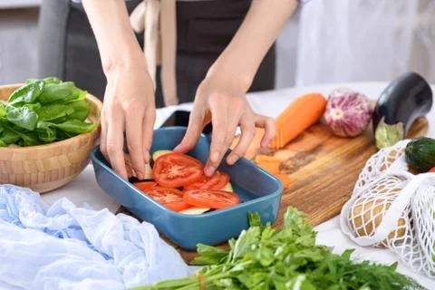 Process of cooking vegetables with hands, tomatoes placed in baking dish, veg Stock Photos