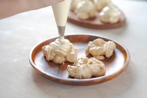 The process of creating Pavlova dessert, decorating the meringue with cream f Stock Photos