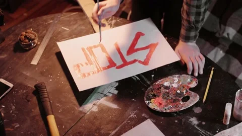 Process of creating protest banner. Man in shirt writes stop sing with red paint Stock Footage 143784946