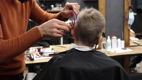 The process of cutting a blond boy with a long braid in a chair in a barbershop Stock Footage 146663598