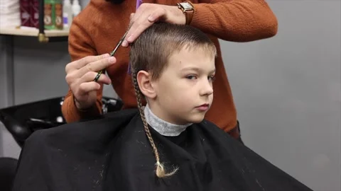 The process of cutting a blond boy with a long braid in a chair in a barbershop Stock Footage 146688592