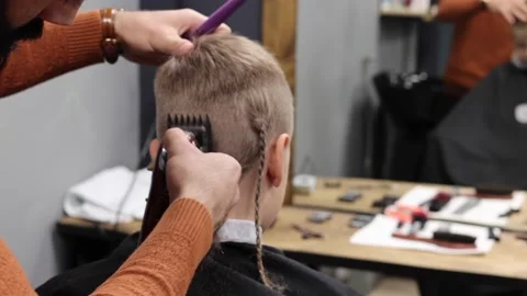 The process of cutting a blond boy with a long braid in a chair in a barbershop Stock Footage 146709278
