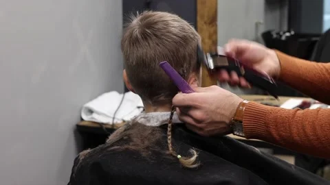 The process of cutting a blond boy with a long braid in a chair in a barbershop Stock Footage 146709291