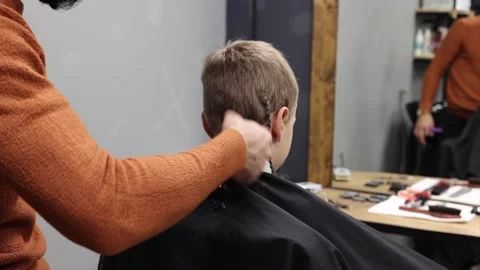 The process of cutting a blond boy with a long braid in a chair in a barbershop Stock Footage 146709307