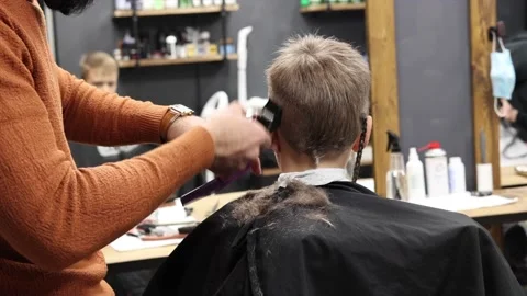 The process of cutting a blond boy with a long braid in a chair in a barbershop Stock Footage 146709335
