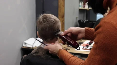 The process of cutting a blond boy with a long braid in a chair in a barbershop Stock Footage 146709348