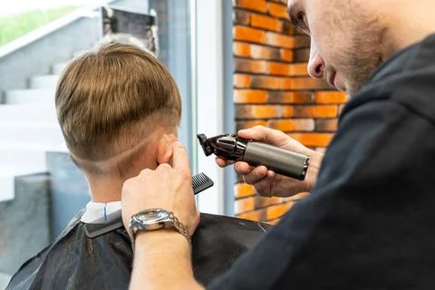The process of cutting a blond boy with a long braid in a chair in a barbershop Stock Photos