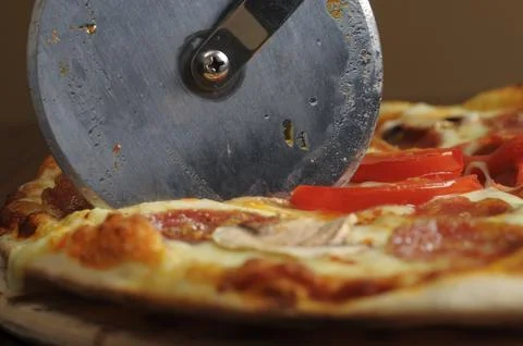 Process of cutting pizza with ham, cheese and tomatoes on a wooden board. Stock Photos