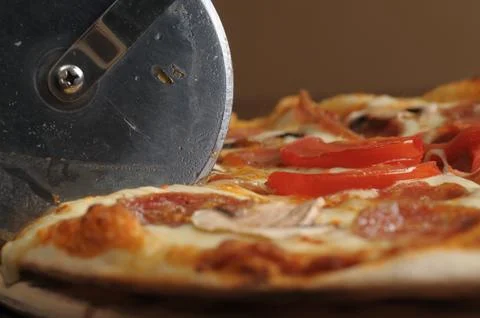 Process of cutting pizza with ham, cheese and tomatoes on a wooden board. Stock Photos