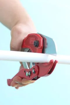 The process of cutting a white plastic pipe with a red pipe cutter Stock Photos