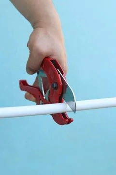 The process of cutting a white plastic pipe with a red pipe cutter Stock Photos