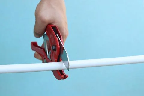 The process of cutting a white PVC pipe with a pipe cutter Stock Photos