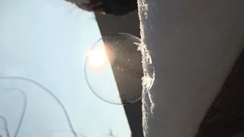 Process of freezing soap bubble in frost on street, in snow in front of the sun Stock Footage 220569194