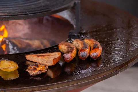 Process of grilling sausages, toast bread slice, pepper on round brazier Stock Photos
