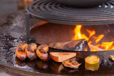 Process of grilling sausages, toast bread slice, pepper on round brazier Stock Photos