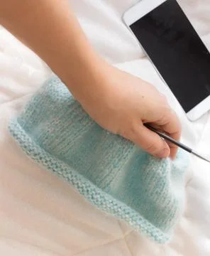 The process of knitting the blue caps from threads on the background of the p Stock Photos