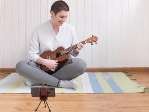 The process of learning to play the guitar online. A brunette girl is sitting Stock Photos