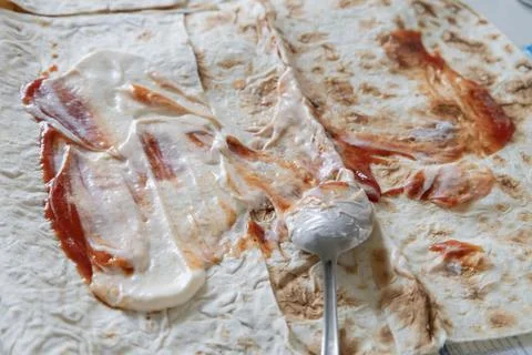 Process of making homemade shawarma: spreading white creamy sauce and red k.. Stock Photos