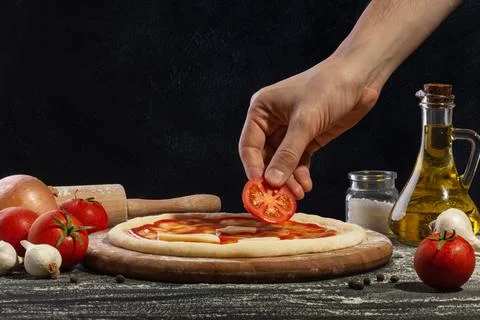 The process of making pizza. A man's hand puts a tomato on a pizza. Stock Photos