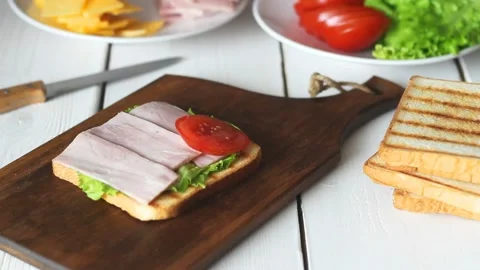 The process of making a sandwich with salad, tomato, ham and cheese. Stock Footage 147848368