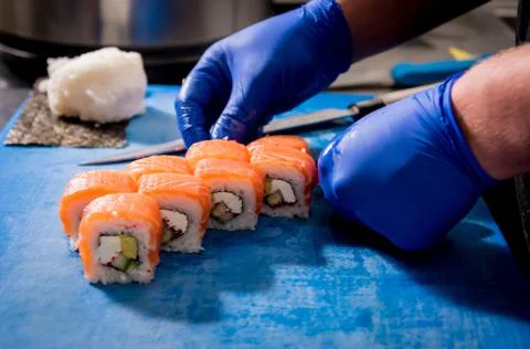 Process of making sushi and rolls at restaurant kitchen. Chefs hands with knife. Stock Photos