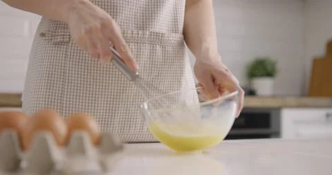Process of mixing eggs with a whisk in a glass bowl on kitchen at home. Woman in Stock Footage 153000067